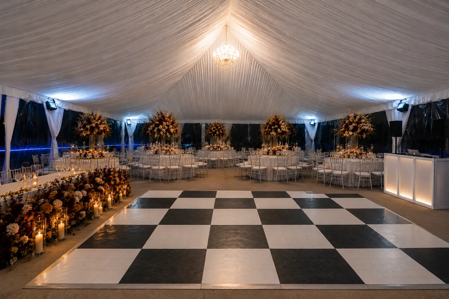 Tented wedding reception with draped ceiling, chandelier, checkered dance floor and burgundy and ivory floral arrangements