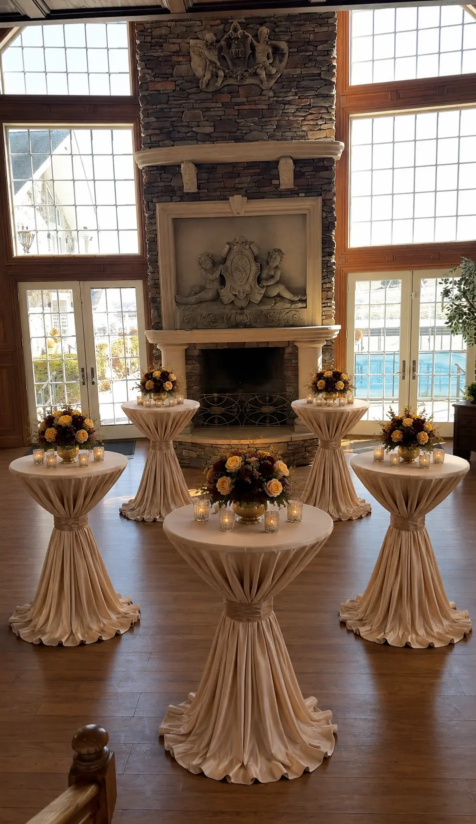 Cocktail hour styling with champagne draped high top tables, autumn floral arrangements and votive candles by a stone fireplace