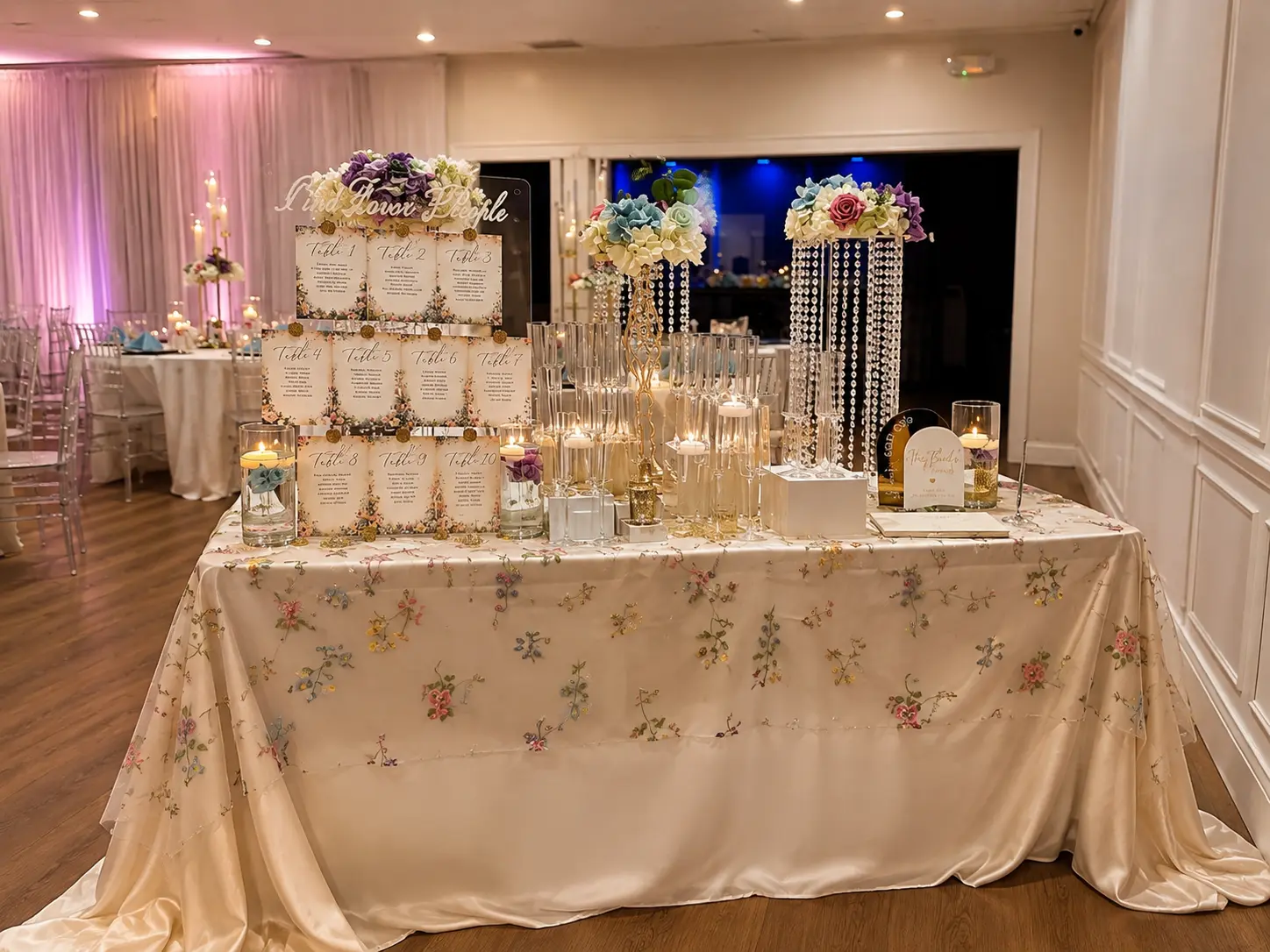Welcome table with a floral seating chart display, crystal draped floral risers, candles and a floral embroidered ivory linen