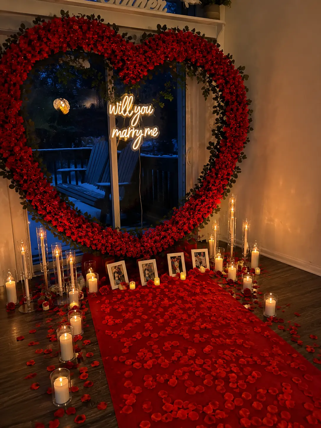 Red rose heart installation with a neon marriage proposal sign above a red petal runner lined with pillar candles