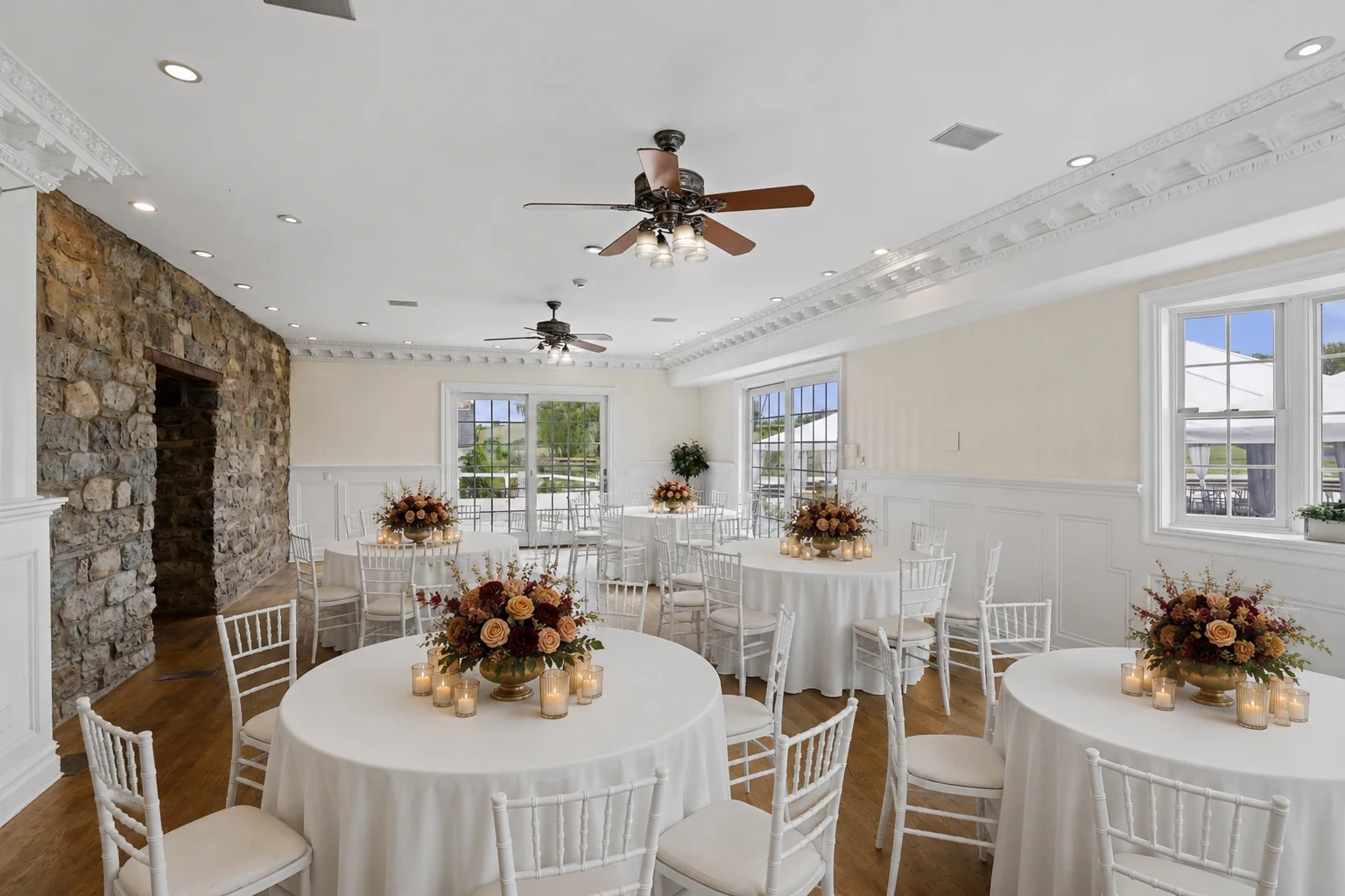 Wedding reception room with round tables, white linens, chiavari chairs and warm floral centerpieces with candles