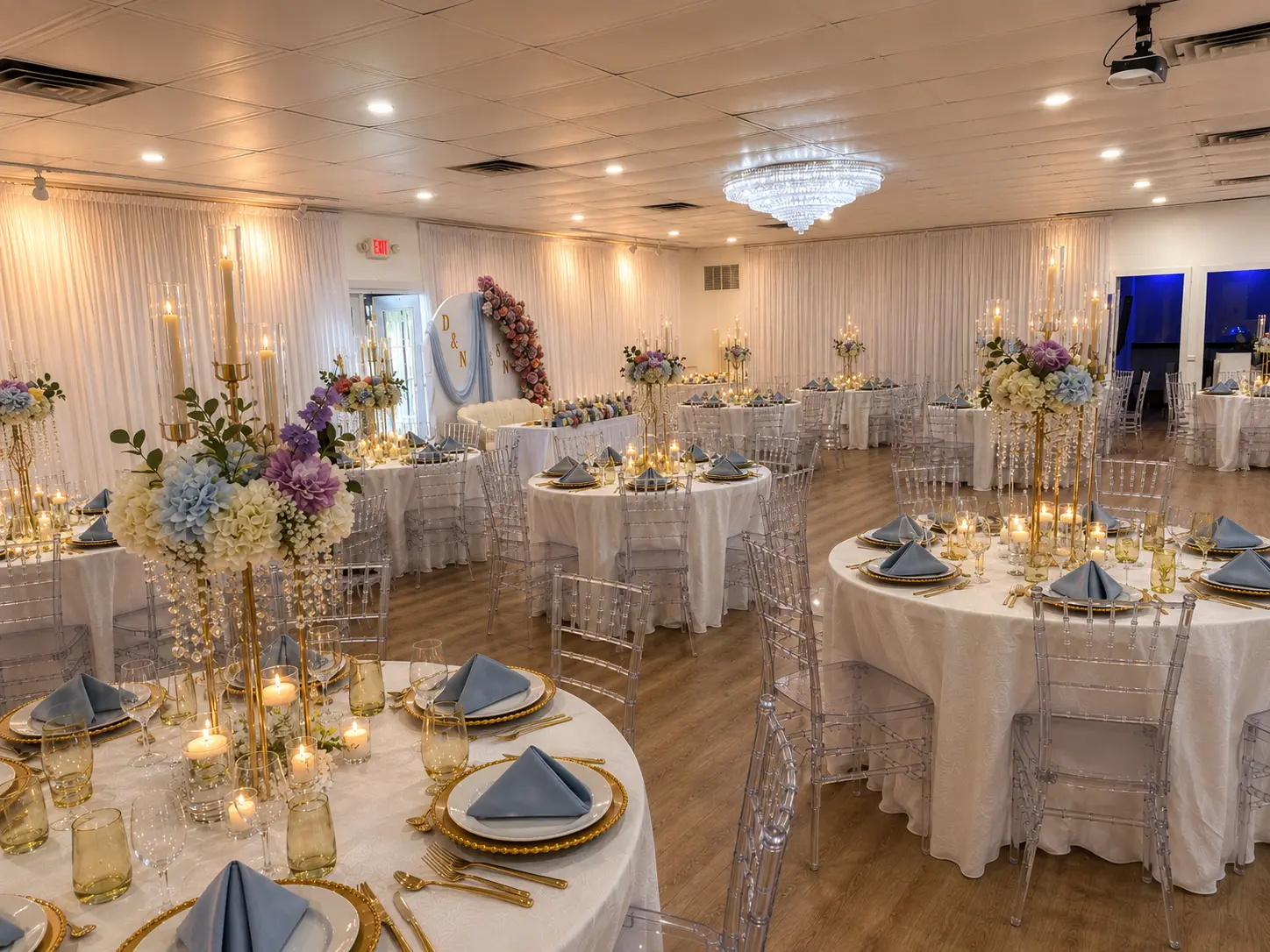 Reception room styled with draped walls, chandelier, candelabras and crystal draped floral centerpieces on round guest tables